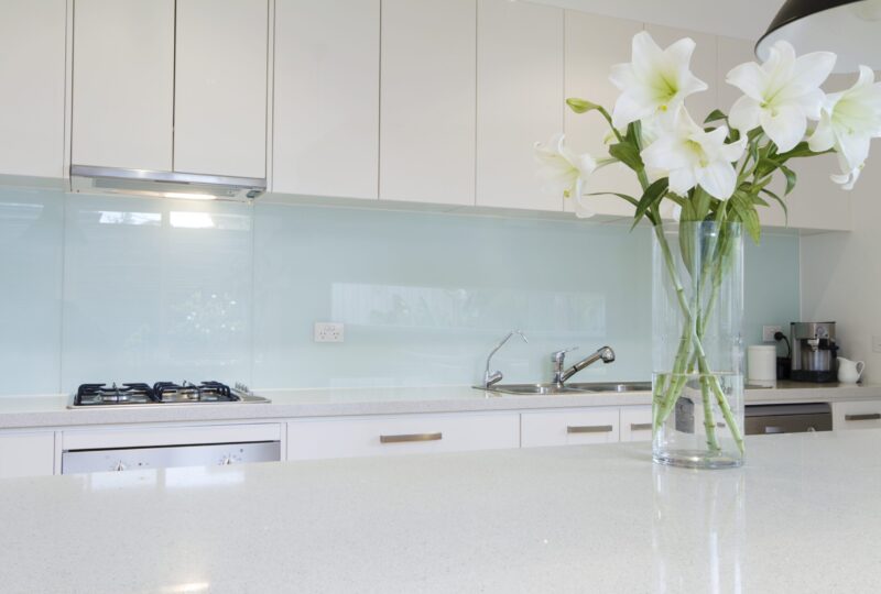 Modern kitchen interior with white cabinets, a gas stove, and a glass vase of white lilies on the countertop.